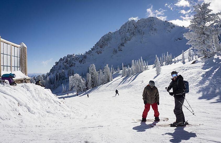 A skier and a snowboarder enjoy the snow and sun at the top of the lift at Snowbasin in Huntsville, Utah.