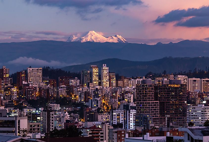 Quito buildings illuminated at dusk with the Antisana volcano in the background. Image Credit Ecuadorpostales via Shutterstock.