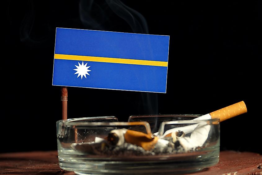 Nauru flag with burning cigarette in ashtray isolated on black background.