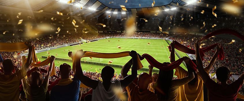 Soccer fans cheering their team with colorful scarfs at crowded stadium at evening time. 