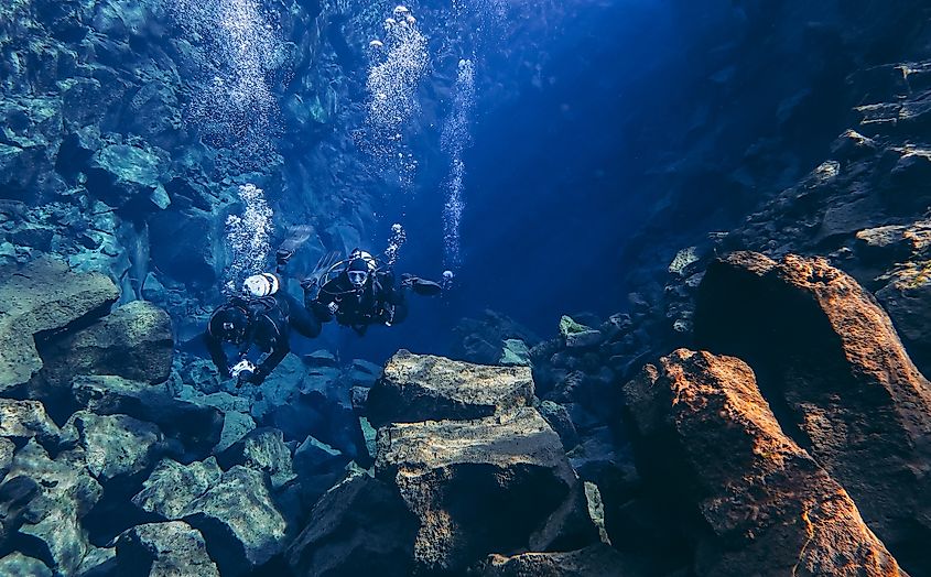 Snorkelers and scuba divers swimming in famous Silfra fissure drift with crystal clear glacial water between tectonic plates, Thingvellir, Iceland.