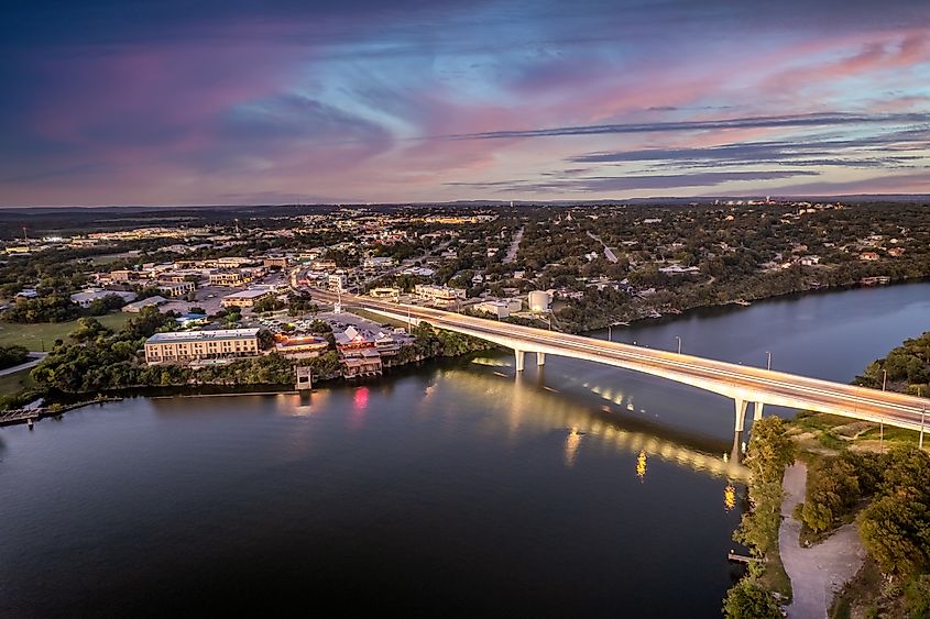 Aerial view of Marble Falls Bridge in Texas at sunset, with the bridge spanning the river and the sky illuminated in vibrant colors.