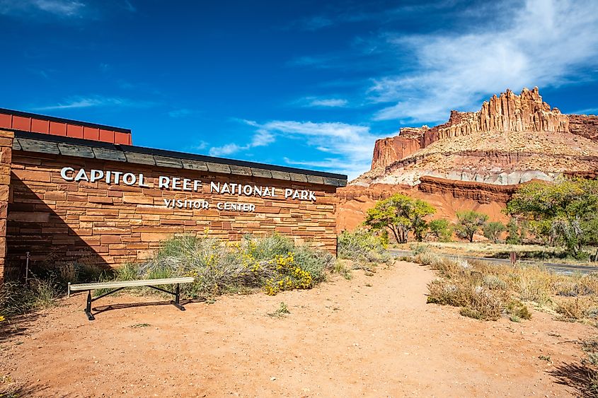 Capitol Reef National Park sign at the visitors center in Torrey, Utah, with red rock formations in the background.