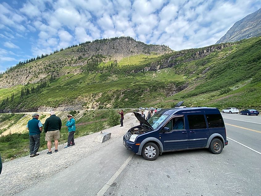 A small blue van with hood popped on the side of the mountainous Going-to-the-Sun Road in Montana.