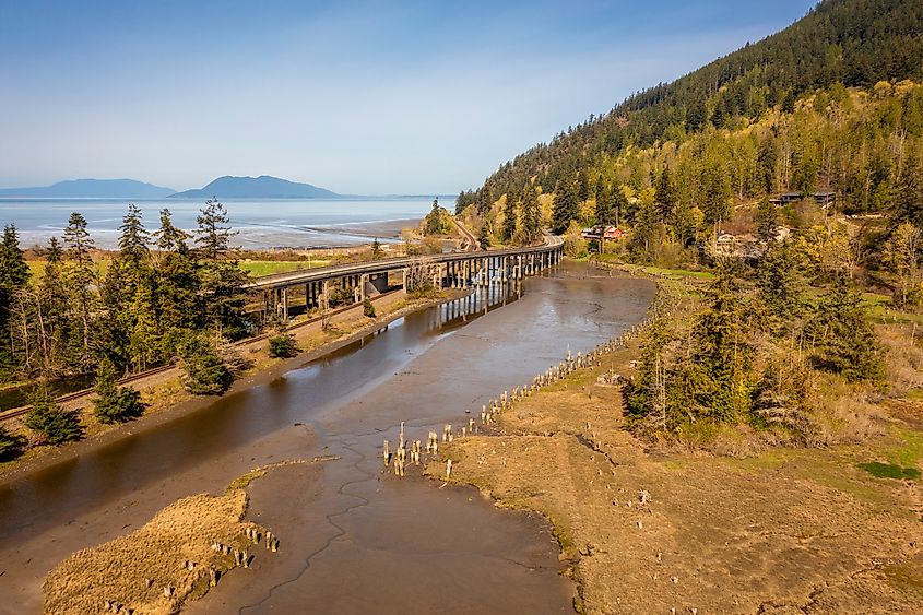 Aerial view of Chuckanut Drive winding along the coastline and crossing the Blanchard Bridge in the Skagit Valley, surrounded by lush greenery and scenic water views.