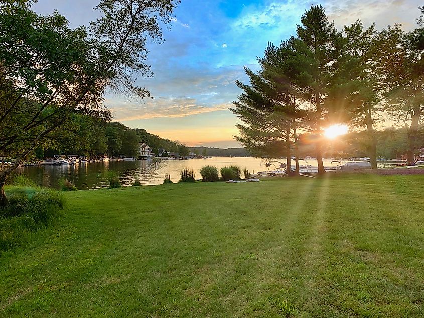 Sunset over Lake Harmony, Pennsylvania, with sun peeking through trees and reflecting off the water against a blue sky.