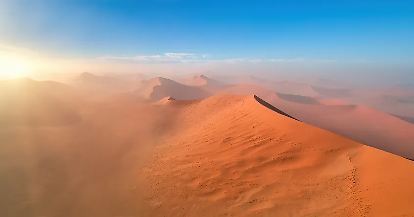 Aerial view of the vast orange dunes of the Namib Desert lit by sunrise.