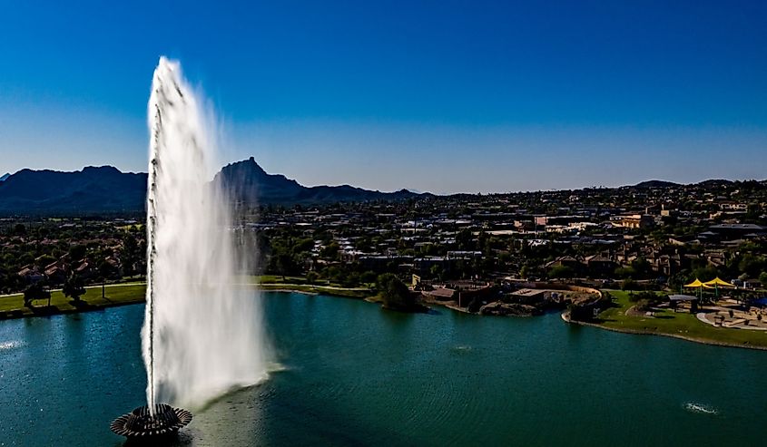 Aerial, drone, view of the Fountain Hills Park Fountain in Fountain Hills, Arizona with blue water, clear sky and landmark mountains