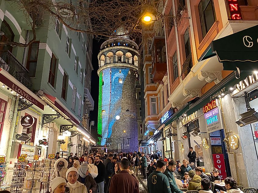 A crowded commercial street in Istanbul, leading to the blue and green-lit, 14th-century Galata Tower.