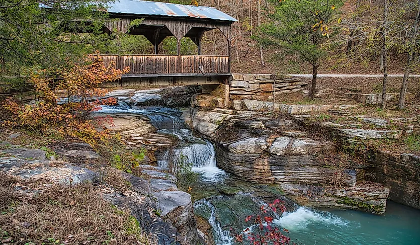 Quaint-covered bridge over a cascading waterfall in autumn in Ponca, Arkansas