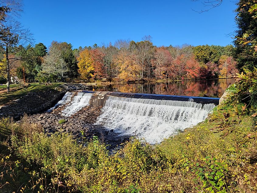 Old Daniels Dam in Killingly, Connecticut, with cascading water flowing over the aged stone structure, surrounded by lush greenery.