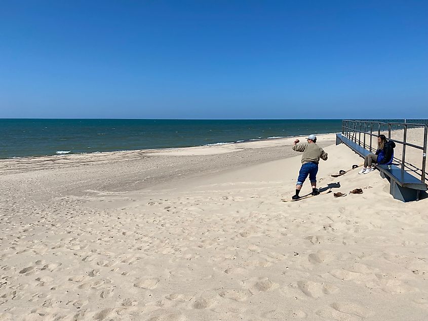 A man sandboards down a small dune, toward the rich blue waters of Lake Michigan