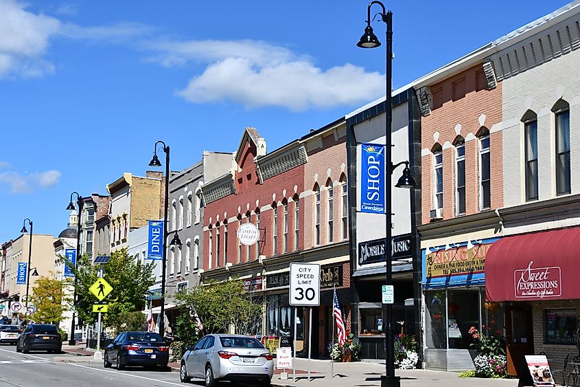 Main Street in downtown Canandaigua, New York, featuring a blend of historic storefronts, shops, and local businesses along a tree-lined street on a clear day.