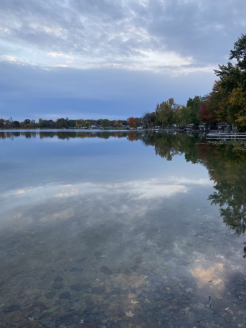 A quiet lake scene at Silver Lake Park with still water reflecting the sky, trees, and nearby houses along the shoreline.