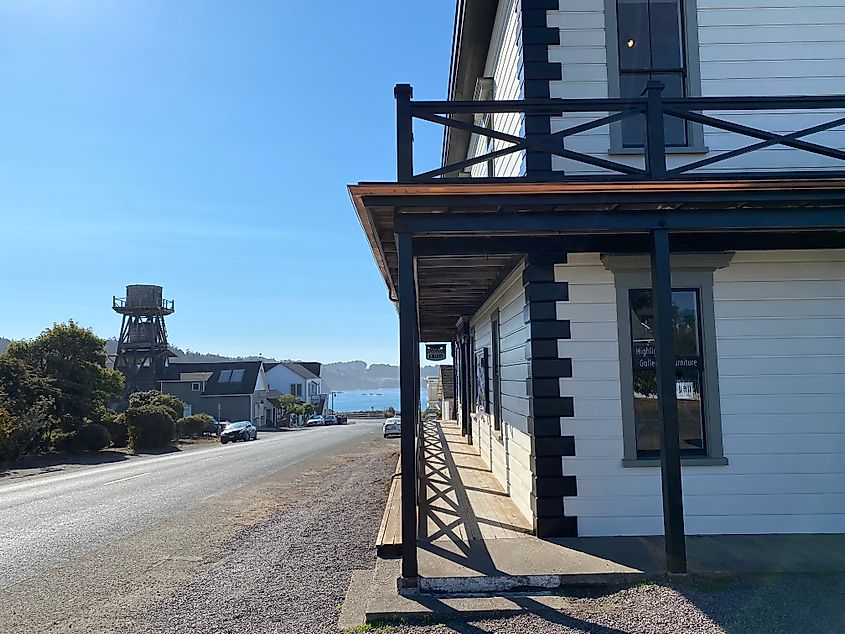 An old fashioned, white-siding commercial building houses a furniture store and art gallery, with a wooden water tower seen in the distance along with a hint of the shimmering Pacific.