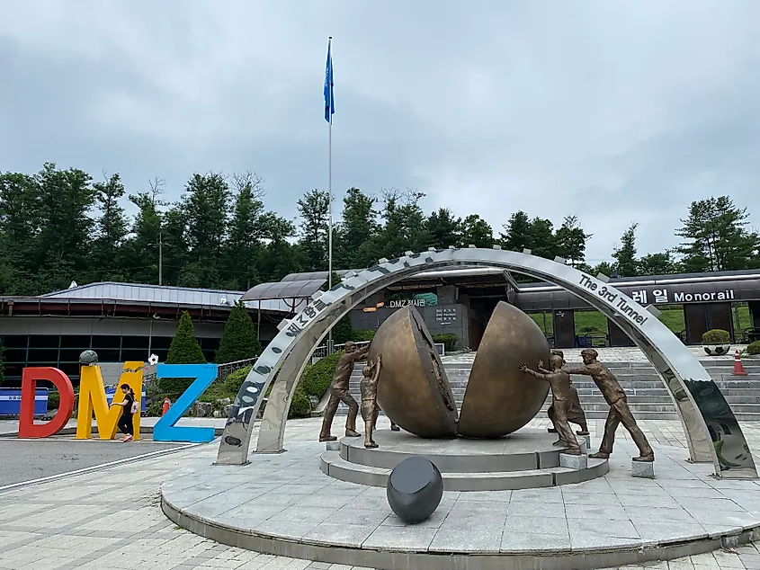 A sculpture depicting people propping up a split world beside DMZ block letters - symbolizing the reunification of Korea.