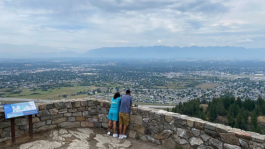 A couple stands atop a viewpoint looking over the mountain town of Kalispell, Montana. 