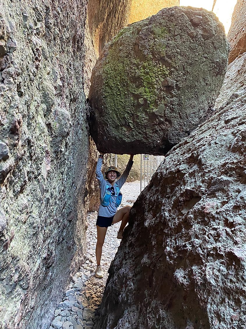 A female hiker pretends to hold up a boulder that is wedged in the narrow slot canyon. 