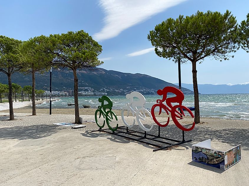 A sculpture of three cyclists marks the start of a mountain backdropped seaside city