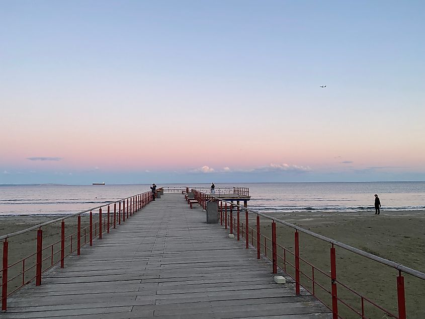 A small beach pier looks out to a pastel sunset over the sea.