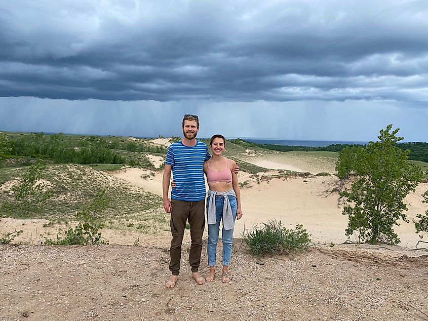 A couple posing atop a large series of sand dunes. Storm clouds are brewing in the background. 