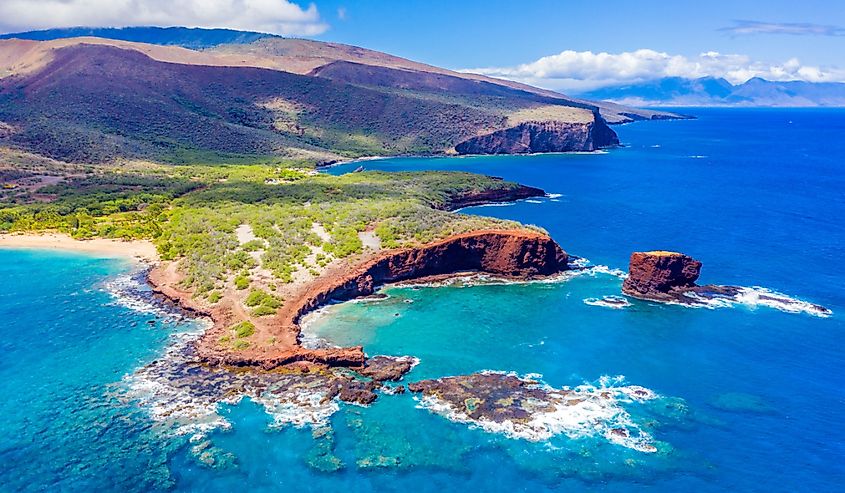 Aerial view of Lanai, Hawaii featuring Hulopo'e Bay and beach, Sweetheart Rock (Pu'u Pehe), Shark's Bay, and the mountains of Maui in the background.