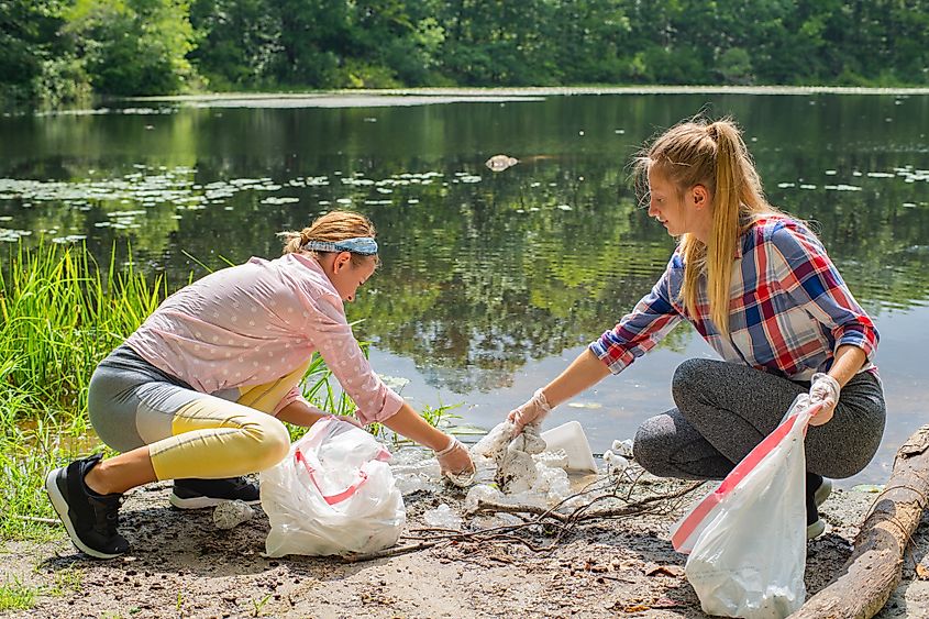 People picking up trash near a lake.
