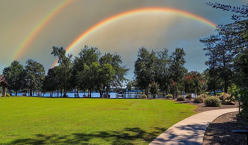 A beautiful summer landscape at Lake Peachtree with lush green grass, trees and plants and blue lake water with blue sky, clouds and a rainbow in Peachtree City, Georgia.