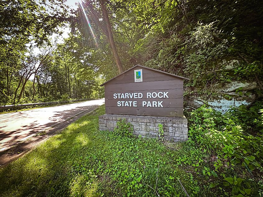 Wooden entrance sign to Starved Rock State Park in LaSalle County, Illinois, surrounded by green grass and leafy trees, creating a welcoming natural setting for visitors.