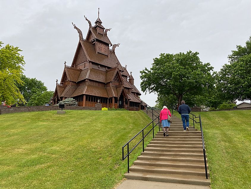 An elderly couple walks up a staircase towards a dramatic, wooden, Norwegian-style cathedral 