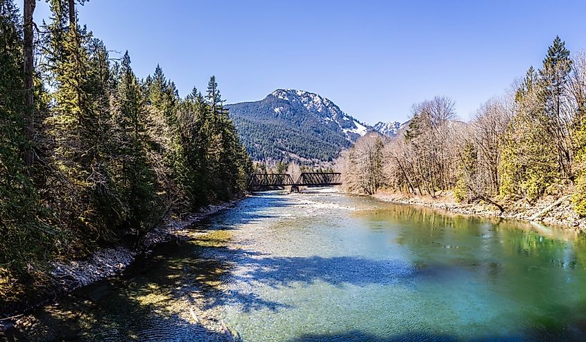 A bridge over the South Fork Skykomish River in Washing State with mountains in the background.