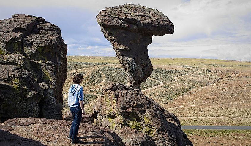 A young woman stands on a rock ledge looking at the famous Balanced Rock near Buhl, Idaho.