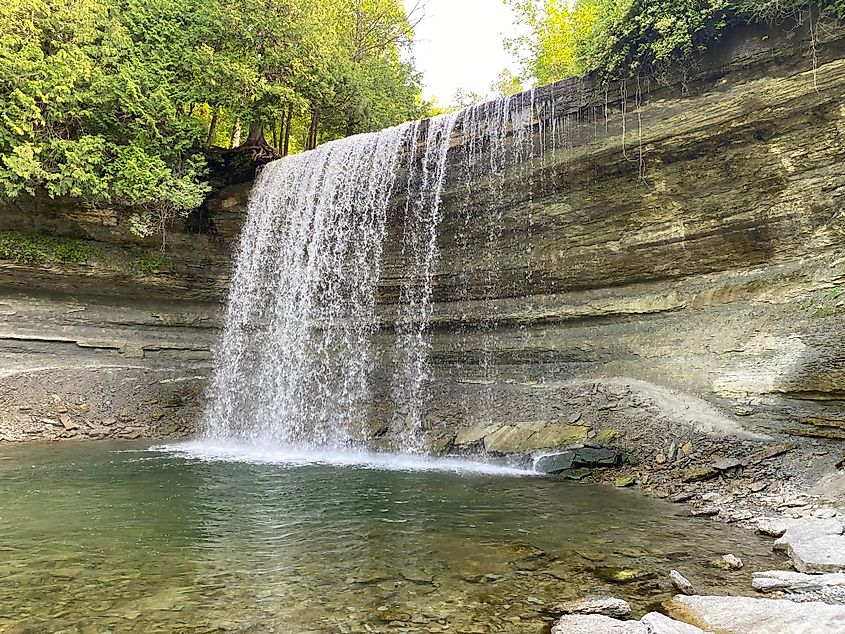 A wide waterfall drops off a rocky cliff into an inviting natural pool