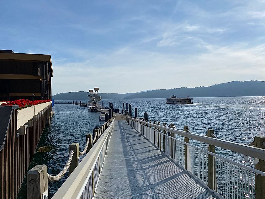 A floating dock leads out into big, blue Lake Coeur d'Alene. A lake cruise boat passes by in the distance. 