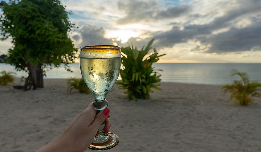 Hand with glass of wine on the beach during sunset. Antigua, Carribean.