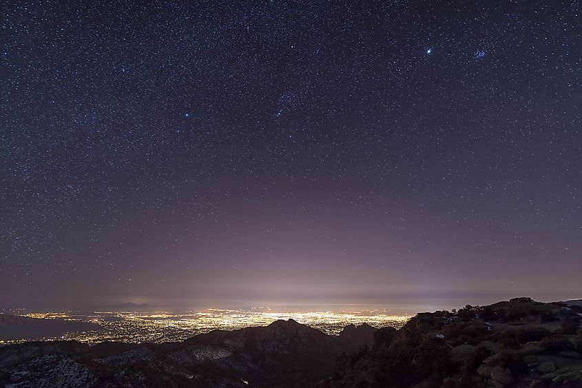 A view from midway up Mount Lemmon, looking down into Tucson, Arizona. Orion, Jupiter, and the Pleiades float above the city lights.