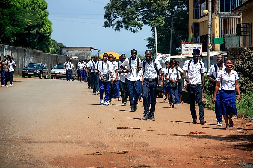 Group of happy teenagers in school uniform walking along a dirt road in Conakry, Guinea. Shutterstock/schusterbauer.com