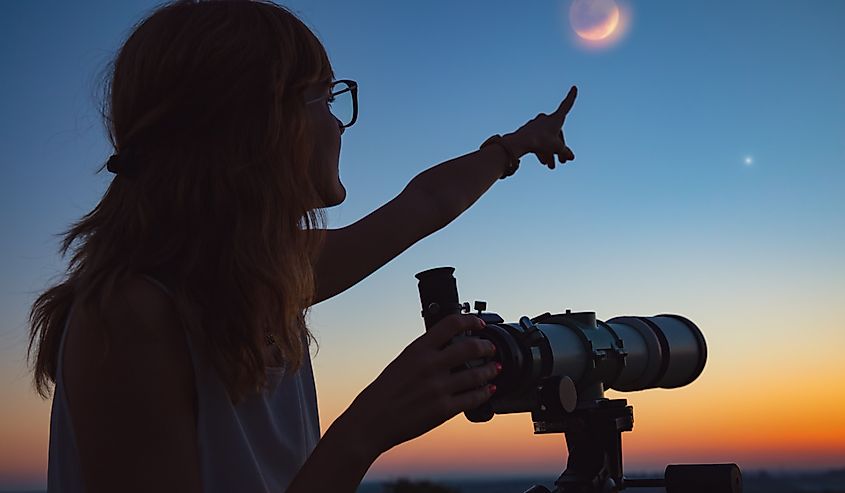 Girl looking at lunar eclipse through a telescope. 