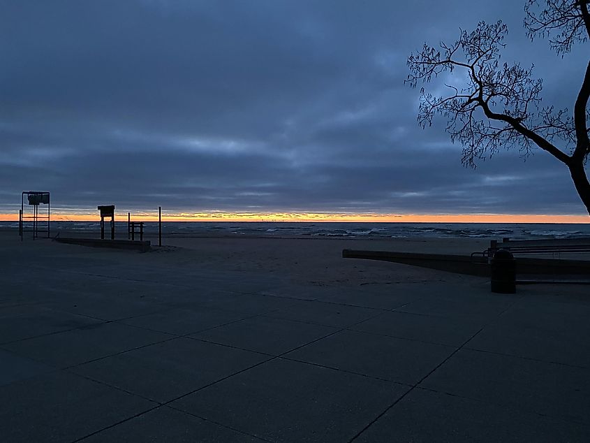 A thin strip of sunset afterglow bisects a cloudy sky and dark wavy waters