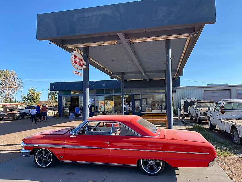 A classic red sports car sits in front of an old gas station, now converted into a coffee shop.