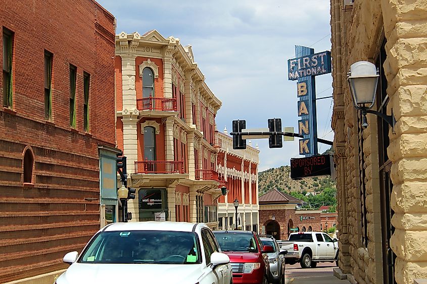 Street view in Trinidad, Colorado, showing historic brick and stone buildings, parked cars, a First National Bank sign, and a traffic signal in a small-town downtown setting.