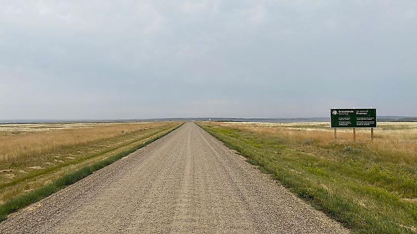 The entrance sign for Grasslands National Park. A long gravel road splits through endless prairie fields. 