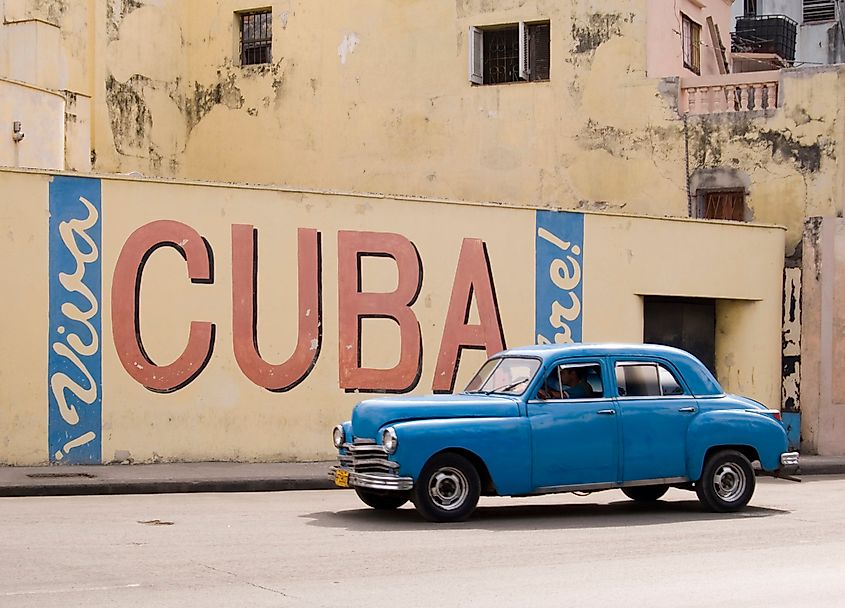 A vintage 1950's american car passing a 'viva Cuba' sign painted on a wall in cental Havana, Cuba.