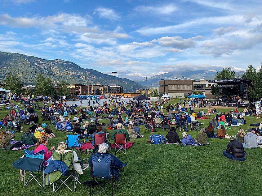 A large crowd gathers before a festival stage with mountains looming in the background.