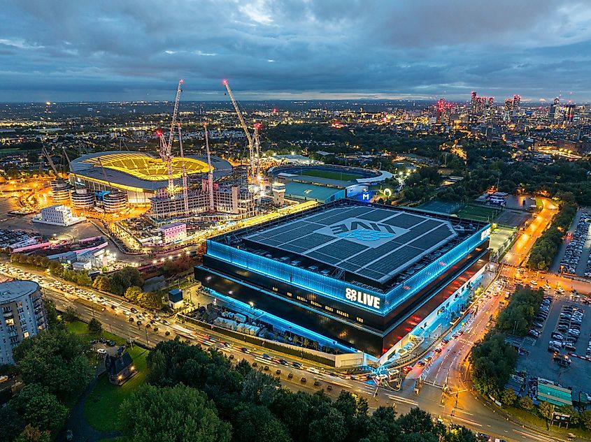 An aerial view of the Co-op Live arena in Manchester at night, illuminated with blue lights and Etihad Stadium