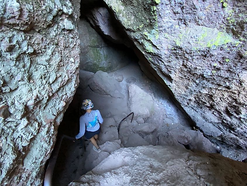 A hiker descends into a dark and steep talus cave. 