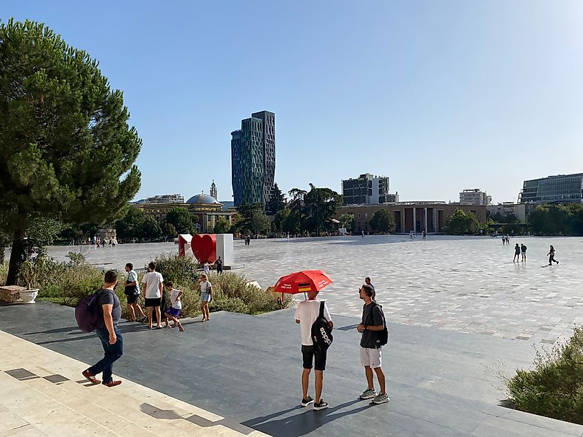 A German tour guide with red umbrella stands before Tirana, Albania's spacious Skanderbeg Square.