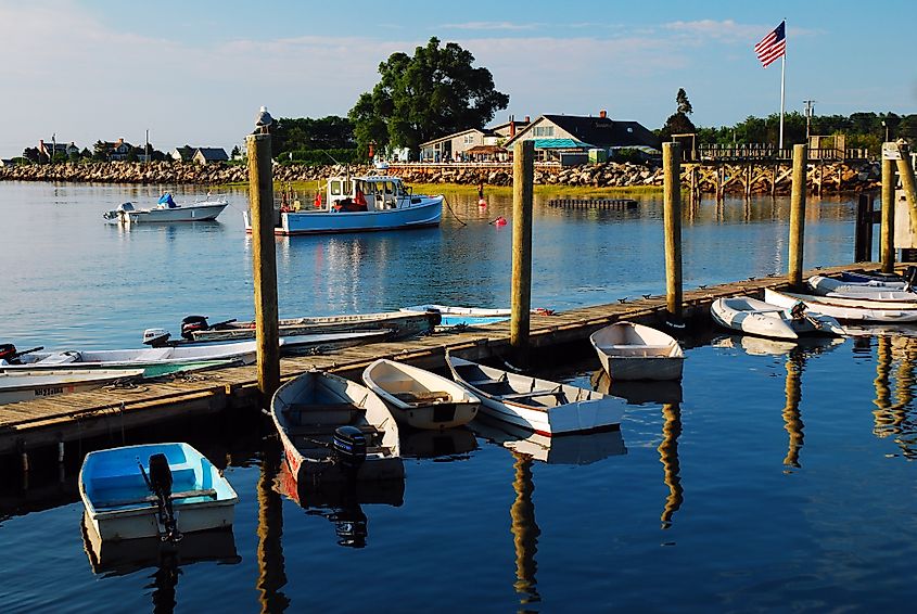 Small dinghies, rowboats, and pleasure craft are moored to a modest dock in calm, reflective water off the coast of Rye, New Hampshire. 