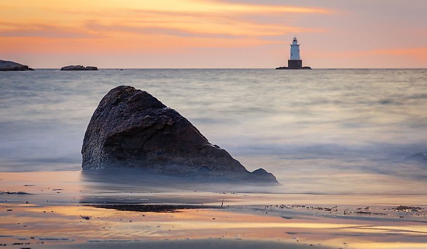 Sakonnet Point lighthouse landscape during golden hour at sunset. The seascape is a long exposure with smooth silky water and rocky foreground.