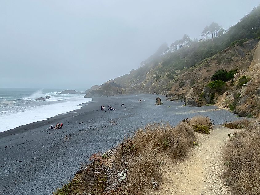 A black sand beach pinched between a sheer cliff and a moody ocean.